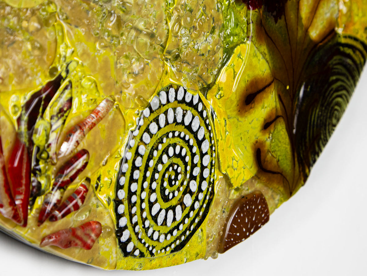 Textural detailing on a fused glass round panel featuring organic autumn inspired patterns and shapes, in a vibrant yellow colour-way, handmade and inspired by the autumnal season. 