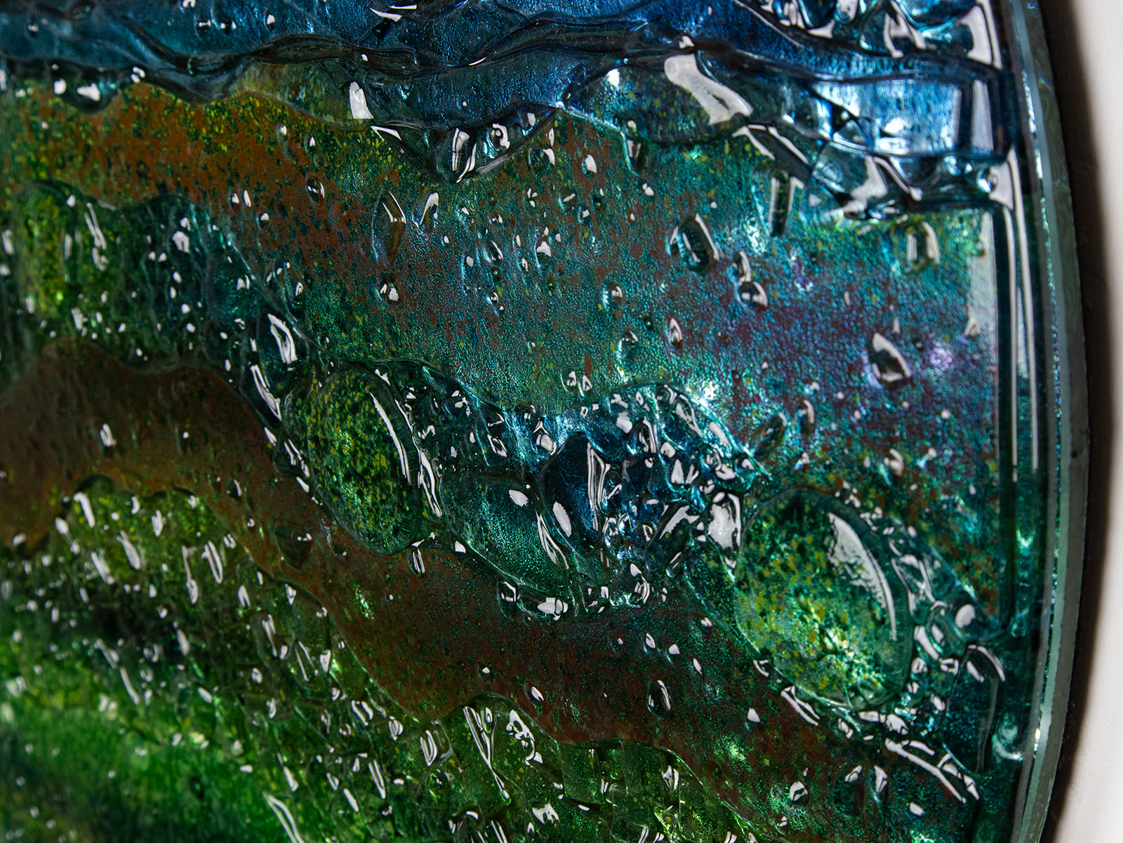 A close up of a round textured glass wall art piece featuring an abstract design with wavy organic hues.