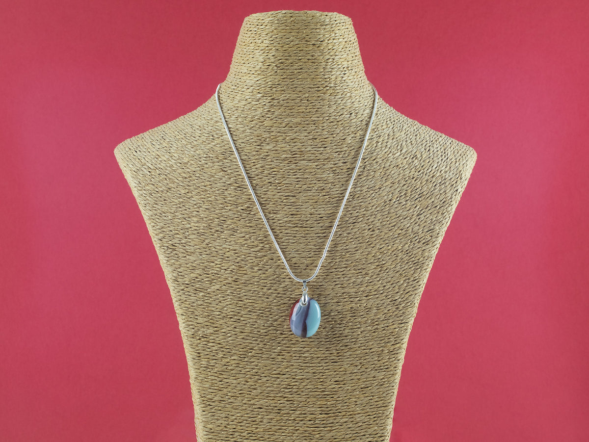 Artisan fused glass pendant necklace, handcrafted in our studio, with delicate blues and a flash of bright red. Finished with a sterling silver chain and fittings, hung on a mannequin. 