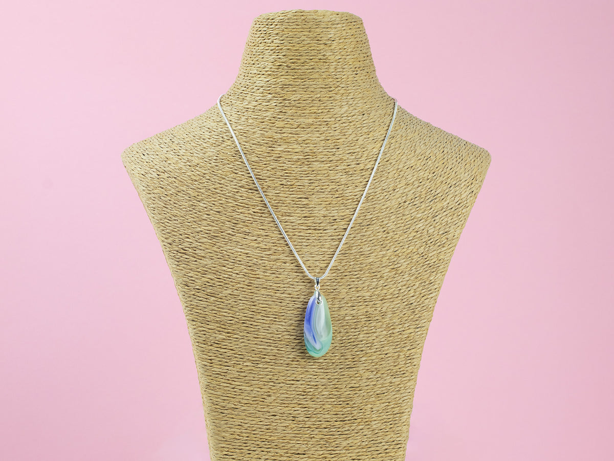 A fused glass teardrop pendant, hung on sterling silver chain in coastal and pink colours and seen on a mannequin.