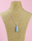 A fused glass teardrop pendant, hung on sterling silver chain in coastal and pink colours and seen on a mannequin.