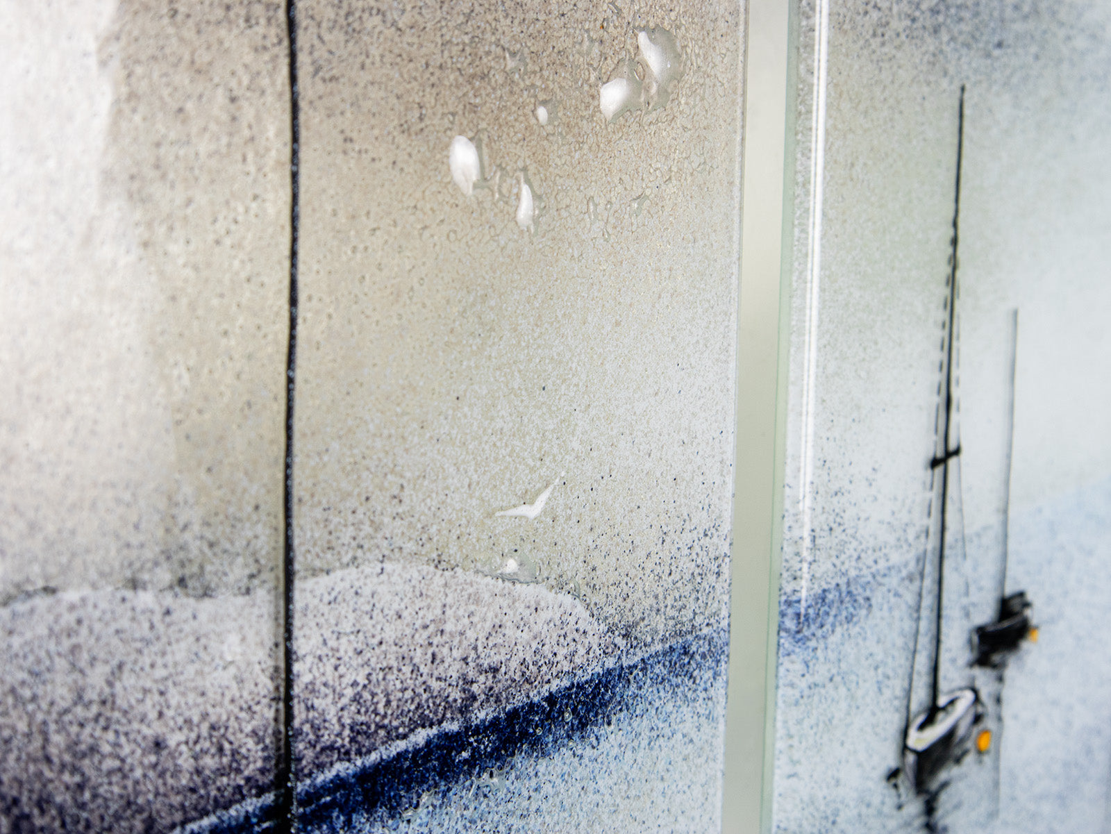 Details on a fused glass staggered triptych featuring a hand-painted sailboat design in a soft and misty colour-way. 