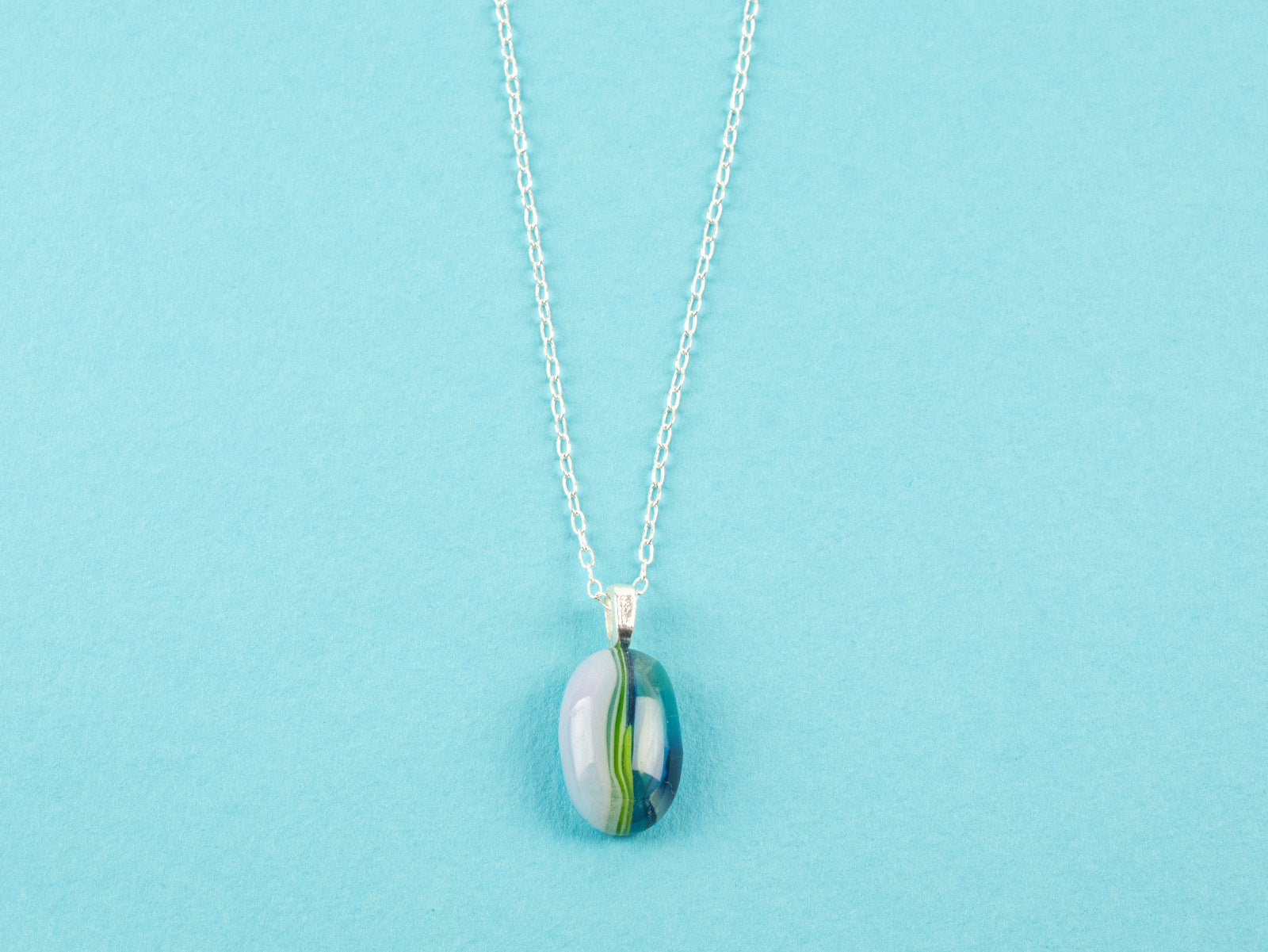 A fused glass pendant necklace on a sterling silver chain, handmade with soft coastal colours.