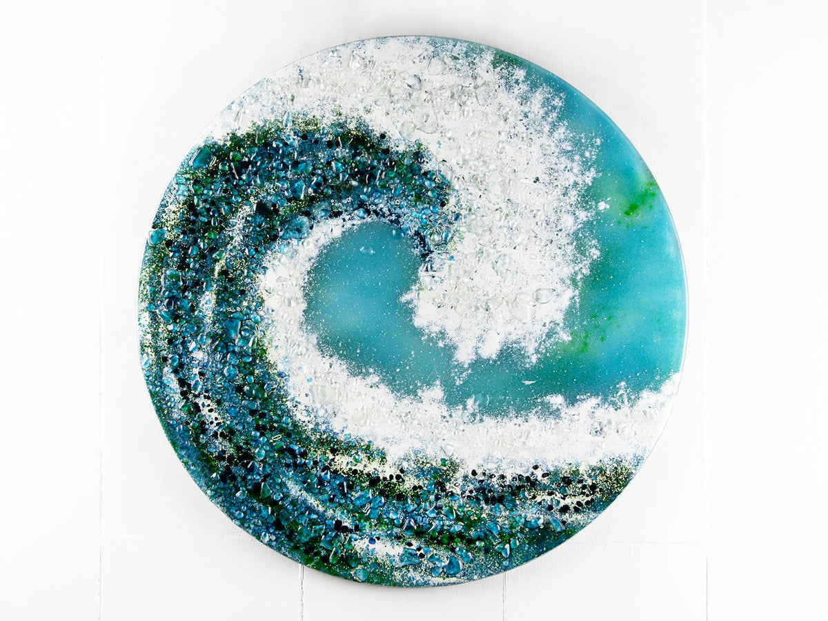 A fused glass round panel in a wave design, handmade with textured teals, whites and aqua tones. 