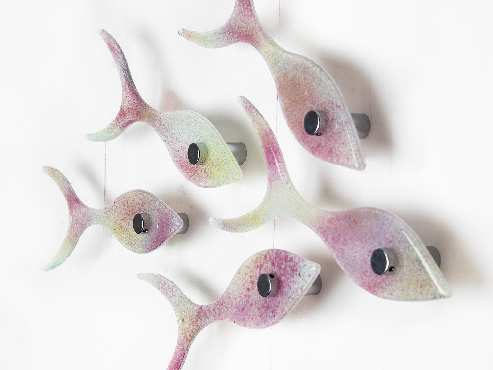 Close up image of a small fused glass shoal of fish, handmade in soft pinks and pearly whites. 