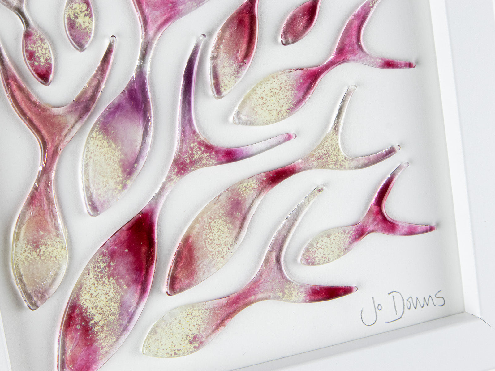 Close up of a signature on an art frame with hand-cut fused glass shoal of fish in a sunset pink colour-way, inspired by the ocean. 