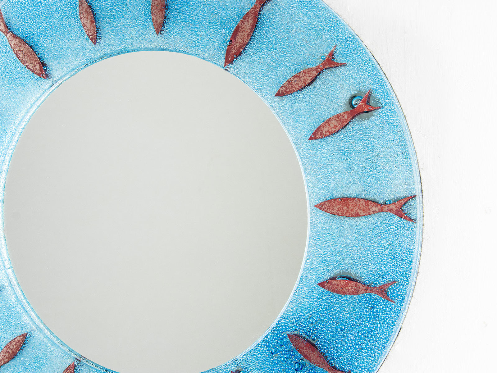 Close up of circular fused glass mirror, featuring circular design of copper fish with an aqua blue colour-way, creating a coastal and ocean inspired wall art design. 