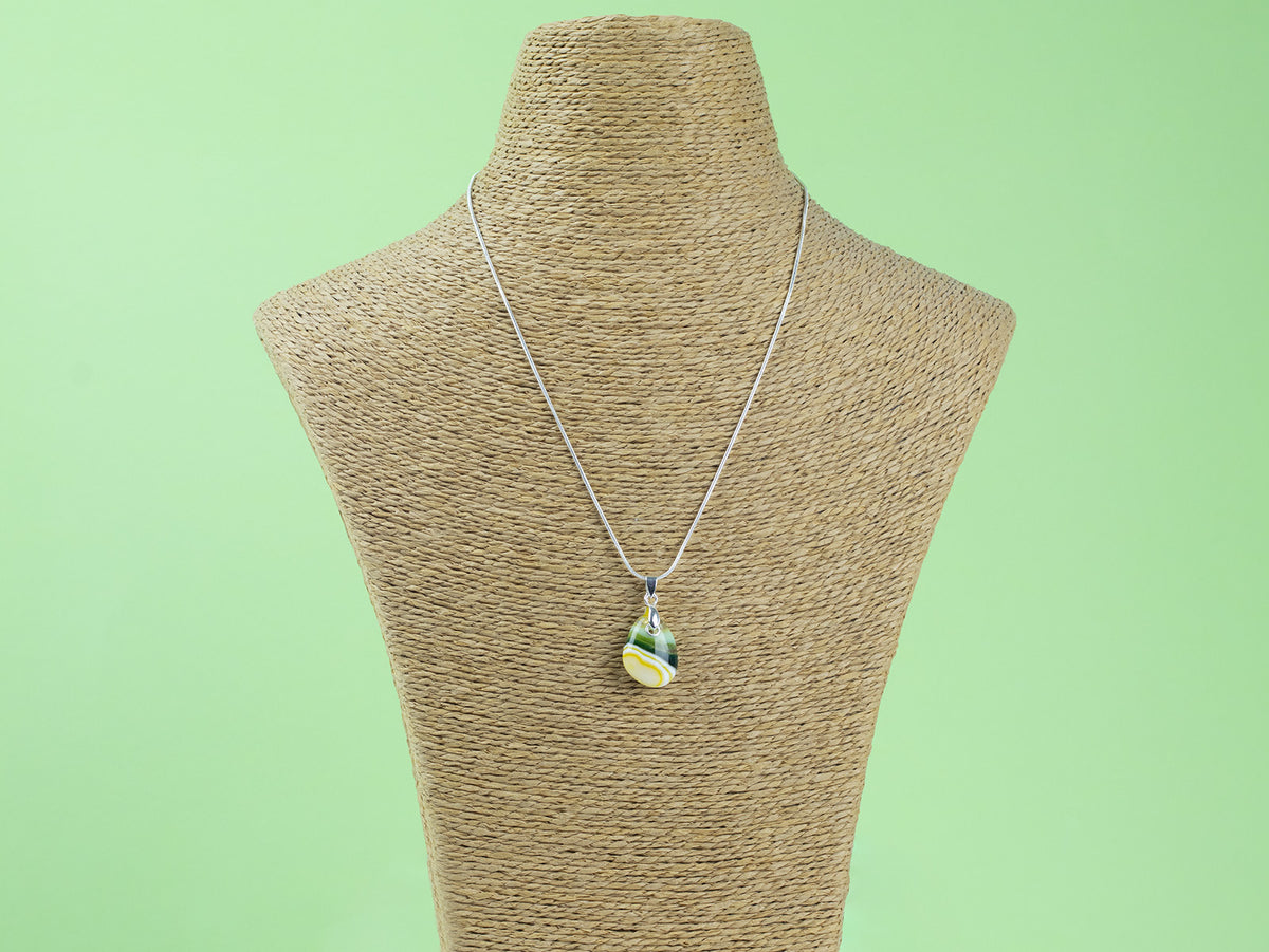 A sterling silver chain necklace with a teardrop-shaped fused glass pendant handmade featuring a golden yellow and sea greens in a marbled design seen on a mannequin. 
