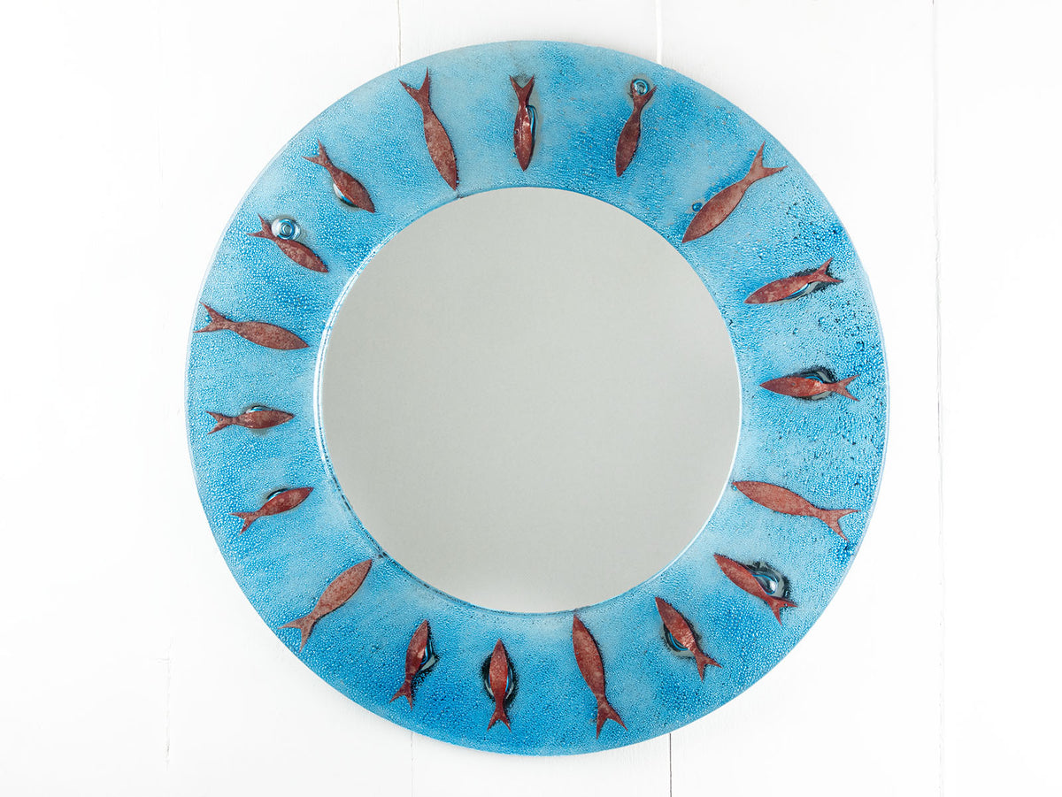 A fused glass round mirror in an aqua colour-way featuring a circular design of copper fish.