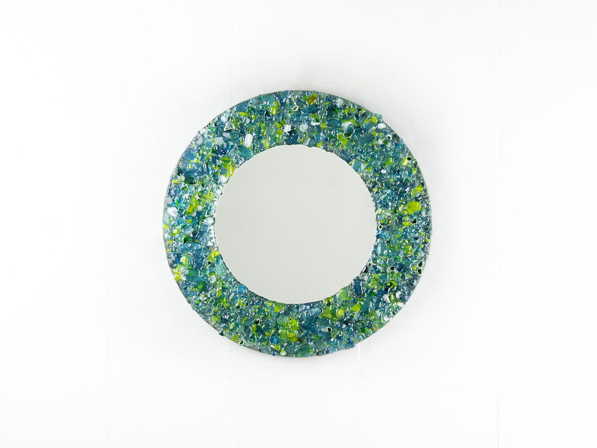 A fused glass round mirror, handmade using recycled ocean coloured glass in green and aqua hues. A coastal inspired piece of wall art. 