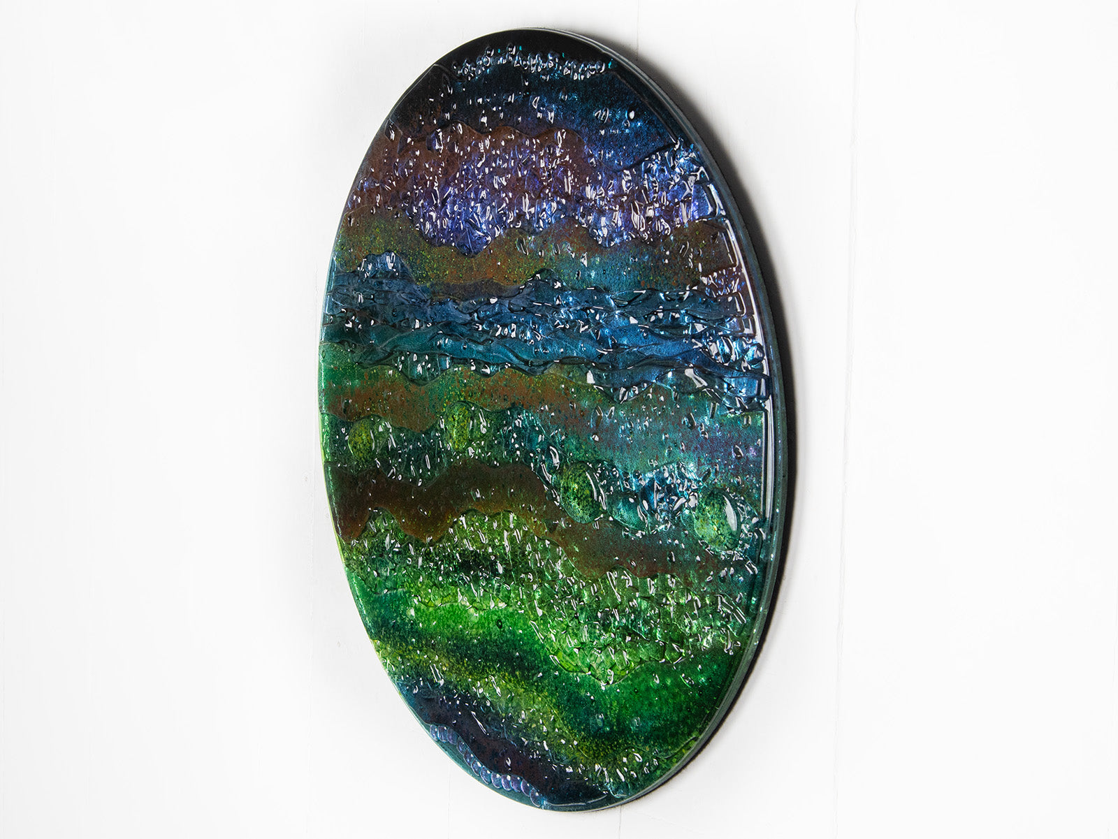 A side image of a round textured glass wall art piece featuring an abstract design with wavy organic hues.