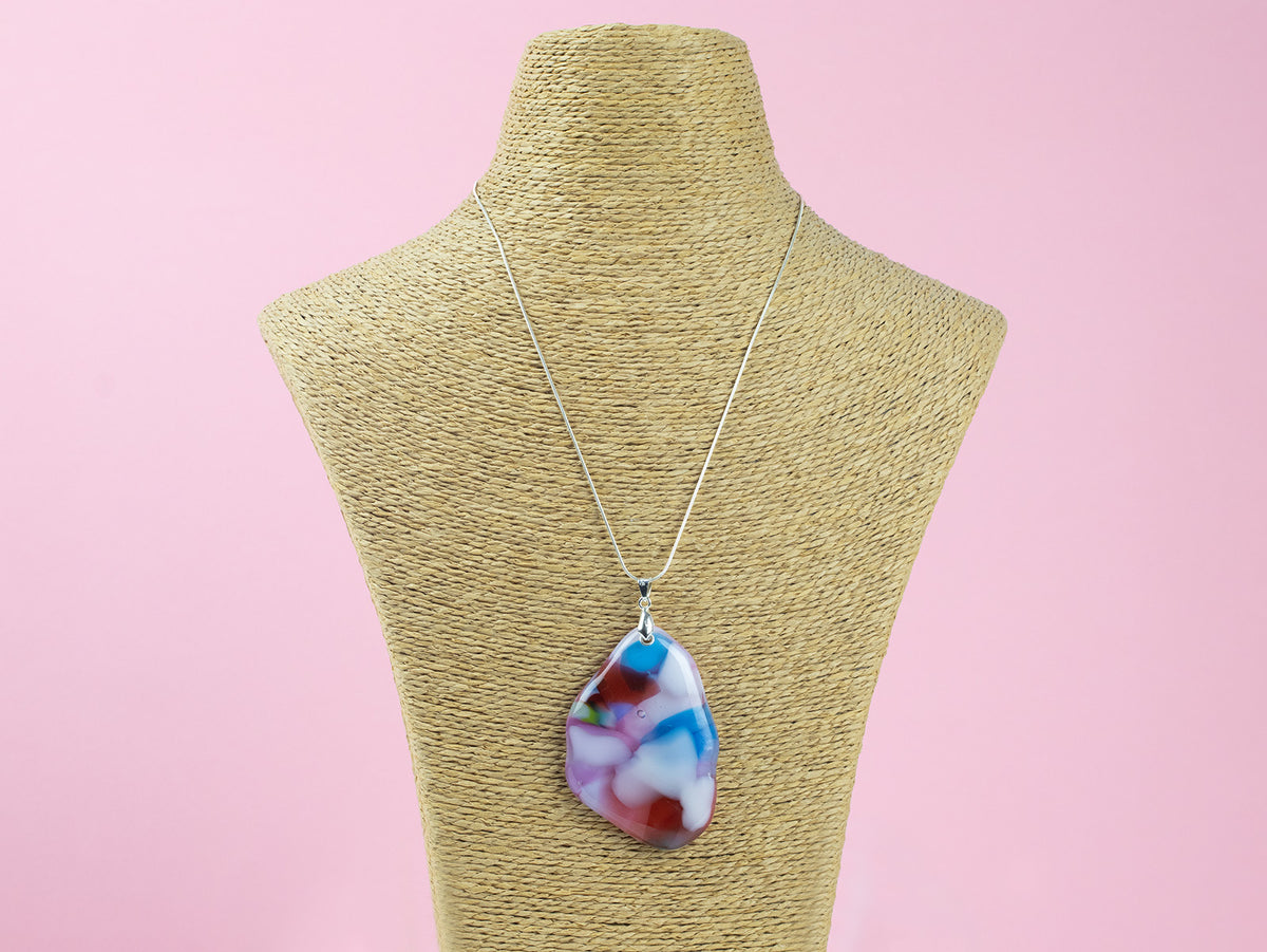 A sterling silver chain necklace with a fused glass pendant featuring a marbled pattern of soft pinks and delicate blue and red hues, seen on a mannequin. 