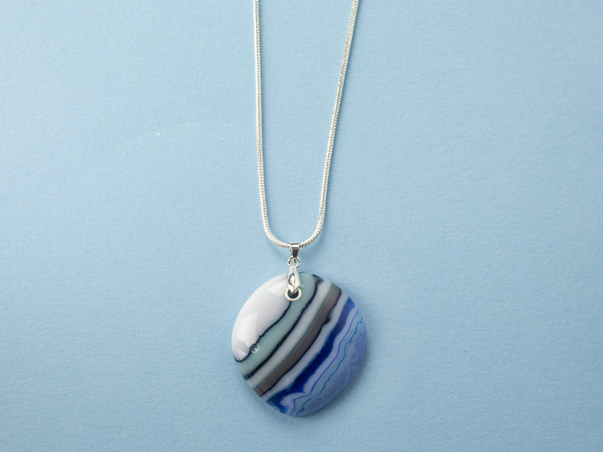 A sterling silver chain necklace with a fused glass pendant featuring a marbled pattern of coastal blues and white. 