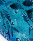 A detailed shot of a round fused glass wall panel featuring hand-cut glass fish and bubbles, designed in a marine blue colour-way.