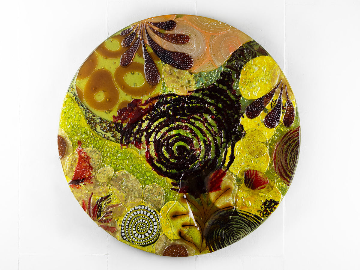 A fused glass round panel featuring organic autumn inspired patterns and shapes, in a vibrant yellow colour-way, handmade and inspired by the autumnal season. 
