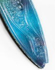 A close up of a surfboard-shaped wall art piece featuring a sea blue and green colour-way with soft waves and textured detailing. 