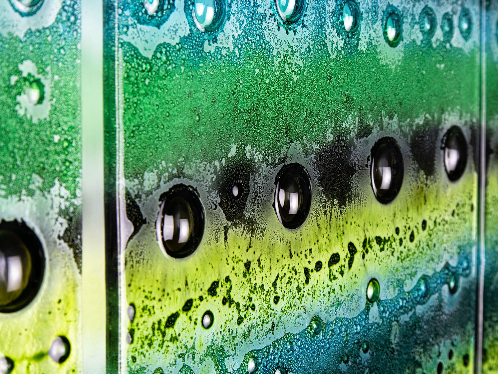 A close up of a fused glass triptych featuring an organic green design with bubbled detailing, handmade in emerald green colours. 