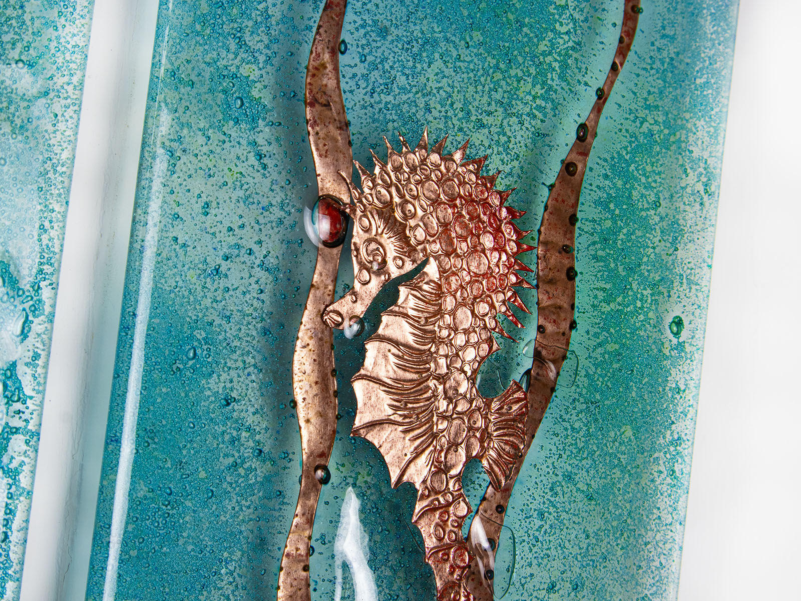 Close up of copper seahorse on a fused glass staggered triptych, with hand-etched copper seahorses and ocean flora and an ocean blue background. 