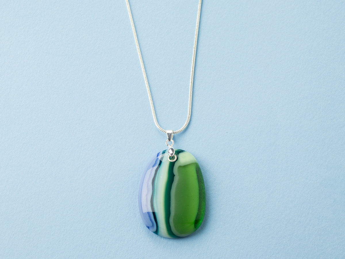 An artisan fused glass pendant necklace, handcrafted in our studio in soft coastal colours. Finished with a sterling silver chain and fittings, designed to be a striking piece of wearable art.