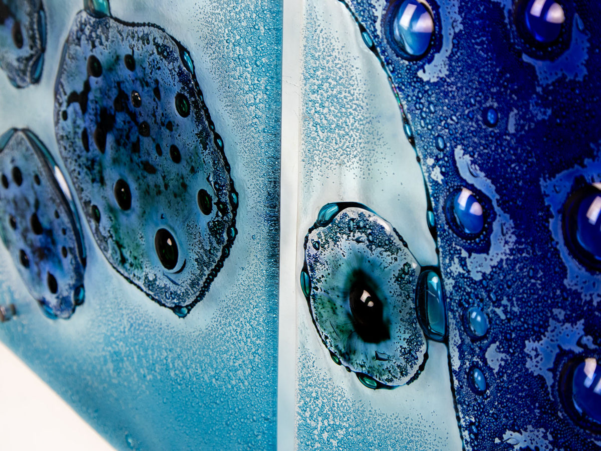 Organic textural detailing on a fused glass staggered triptych wall display, handmade in bright ocean blues and aquas, in a coastal rock-pool design, featuring copper fish. 