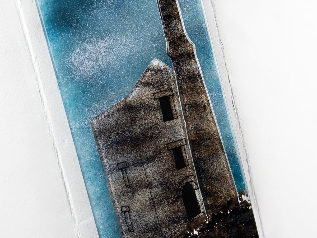 Close up of a fused glass tin mine wall panel set against a moody dark sky, creating a soft Cornish inspired piece of wall art. 