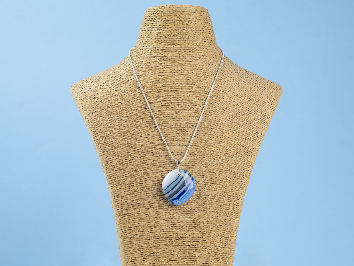 A sterling silver chain necklace with a fused glass pendant featuring a marbled pattern of coastal blues and white, seen on a mannequin. 