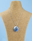 A sterling silver chain necklace with a fused glass pendant featuring a marbled pattern of coastal blues and white, seen on a mannequin. 