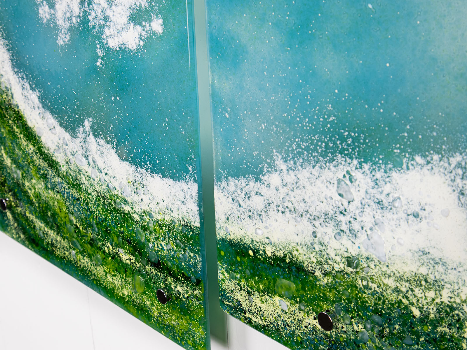 Close up of a fused glass triptych featuring a giant ocean wave, with aqua and sea green colours and white texture. 