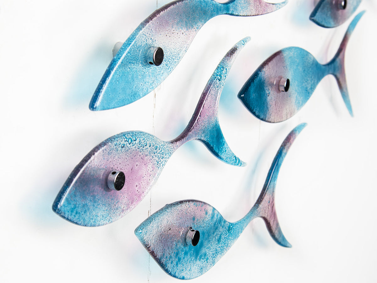 A close up of a fused glass shoal of fish in soft aqua and rose pink hues, creating an ocean inspired wall art installation. 