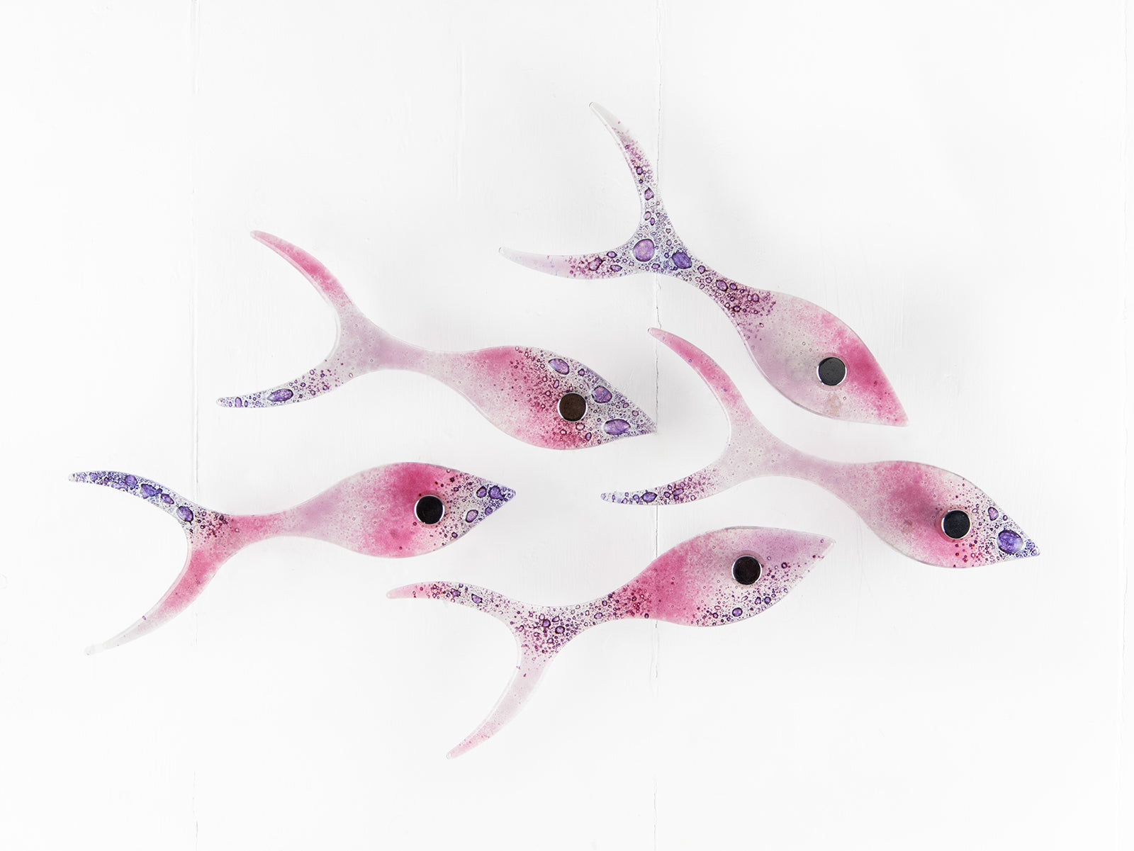 Small fused glass wall display of individual handmade fish in rose pinks and bubbled purple hues. 
