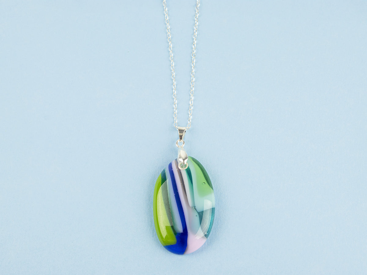 A fused glass pendant necklace, handmade in spring greens, soft pinks and marine blues, hung on a sterling silver chain. 