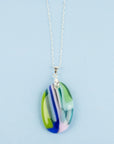 A fused glass pendant necklace, handmade in spring greens, soft pinks and marine blues, hung on a sterling silver chain. 