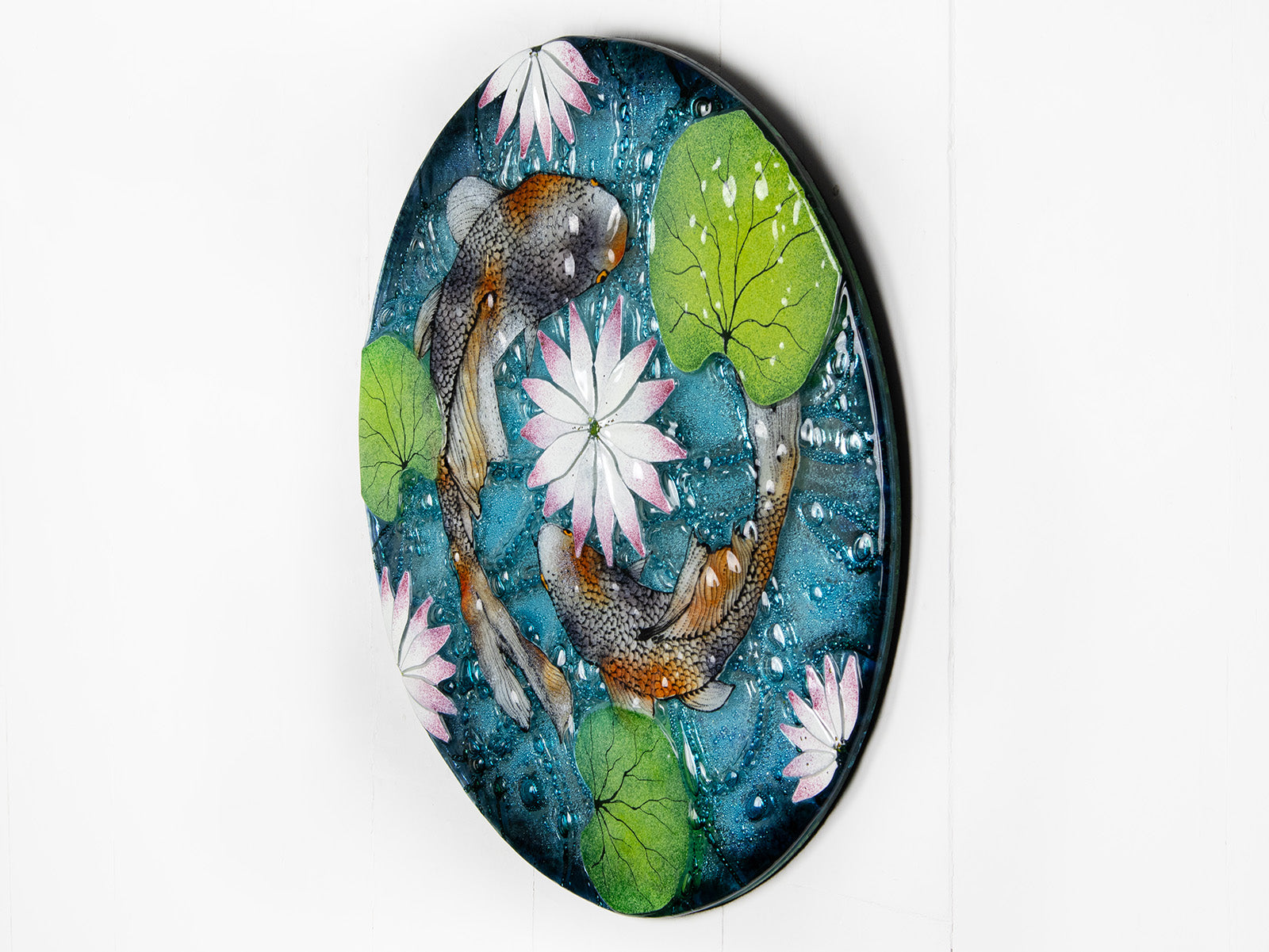 A fused glass round panel featuring hand-painted koi carp design with waterlilies and marine blue background. 
