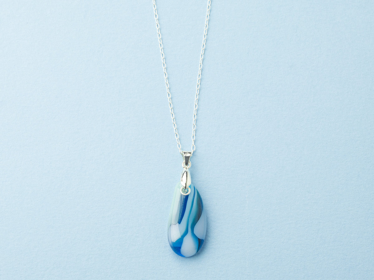 A fused glass pendant necklace, handmade in aqua blue hues, hung on a sterling silver chain. 