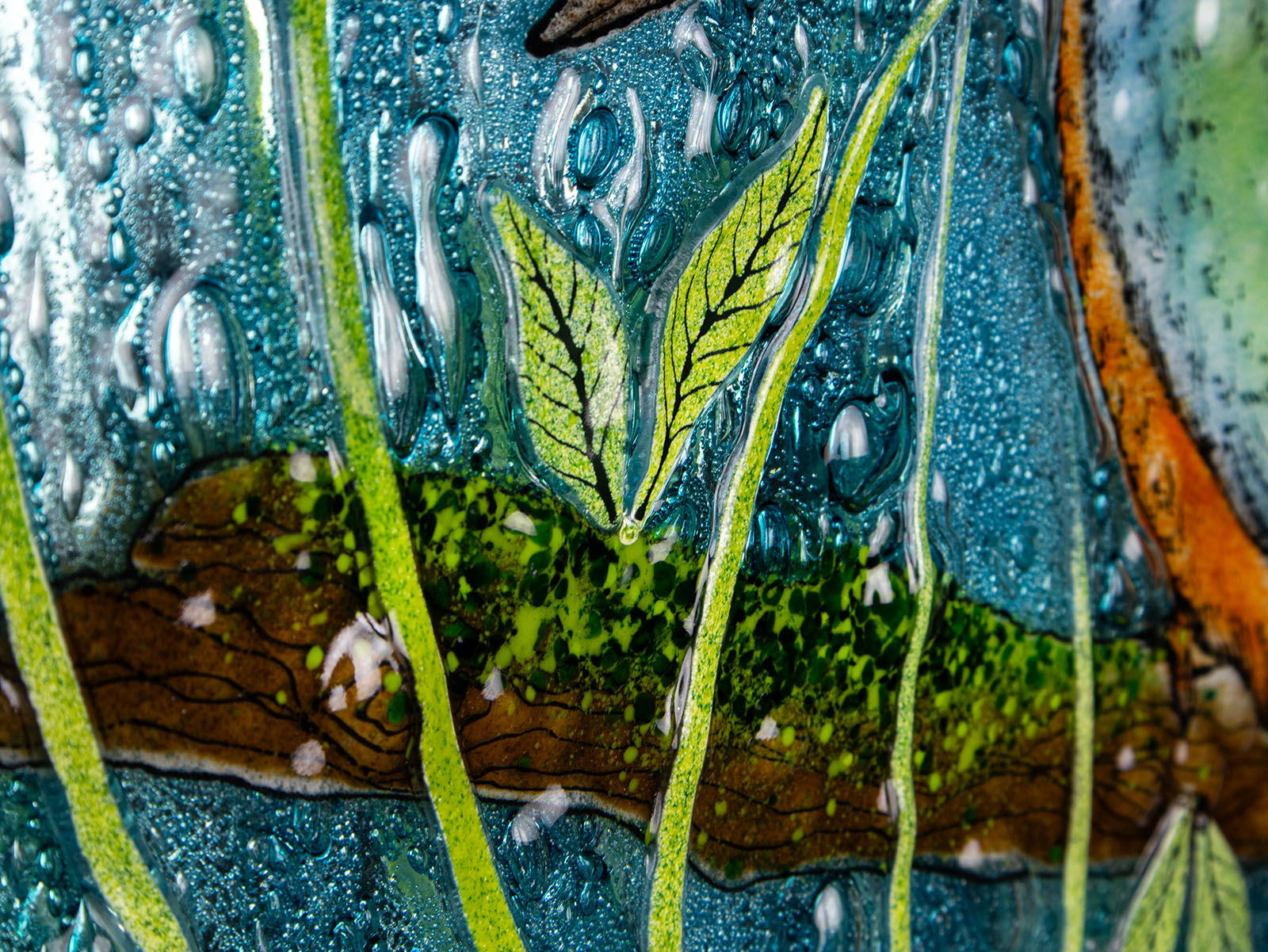 Close up of leaf on a round fused glass wall panel, with hand-painted kingfisher design in vibrant organic colours and textures. 