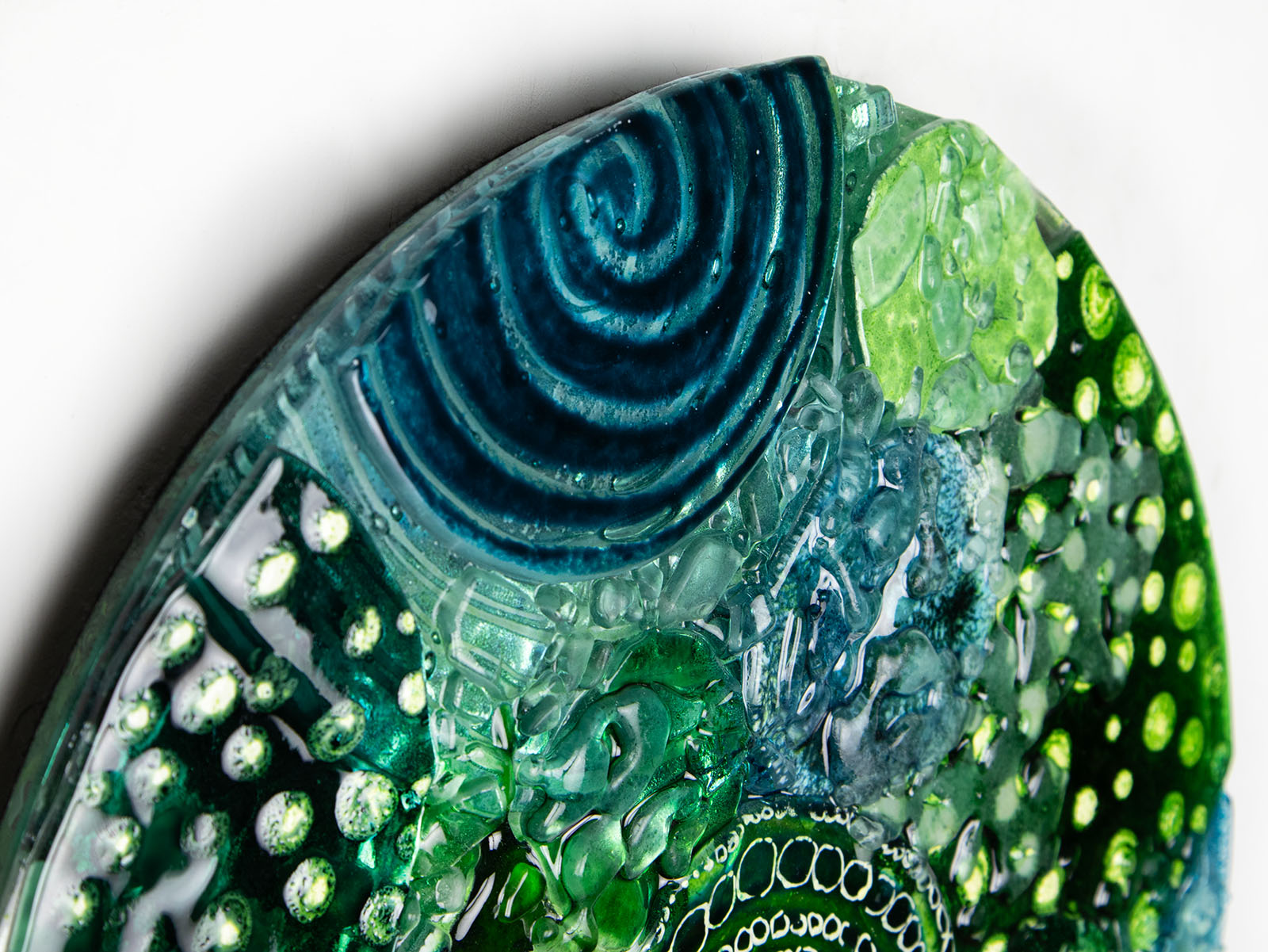 Close up of intricate hand-painted design in ocean colours, handmade in a fused glass wall panel. 
