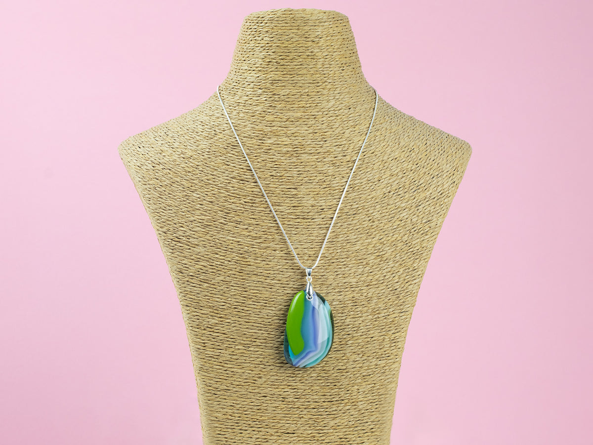 A sterling silver chain necklace with a fused glass pendant featuring a marbled swirl pattern of green, blue, and blushed white, seen on a mannequin. 
