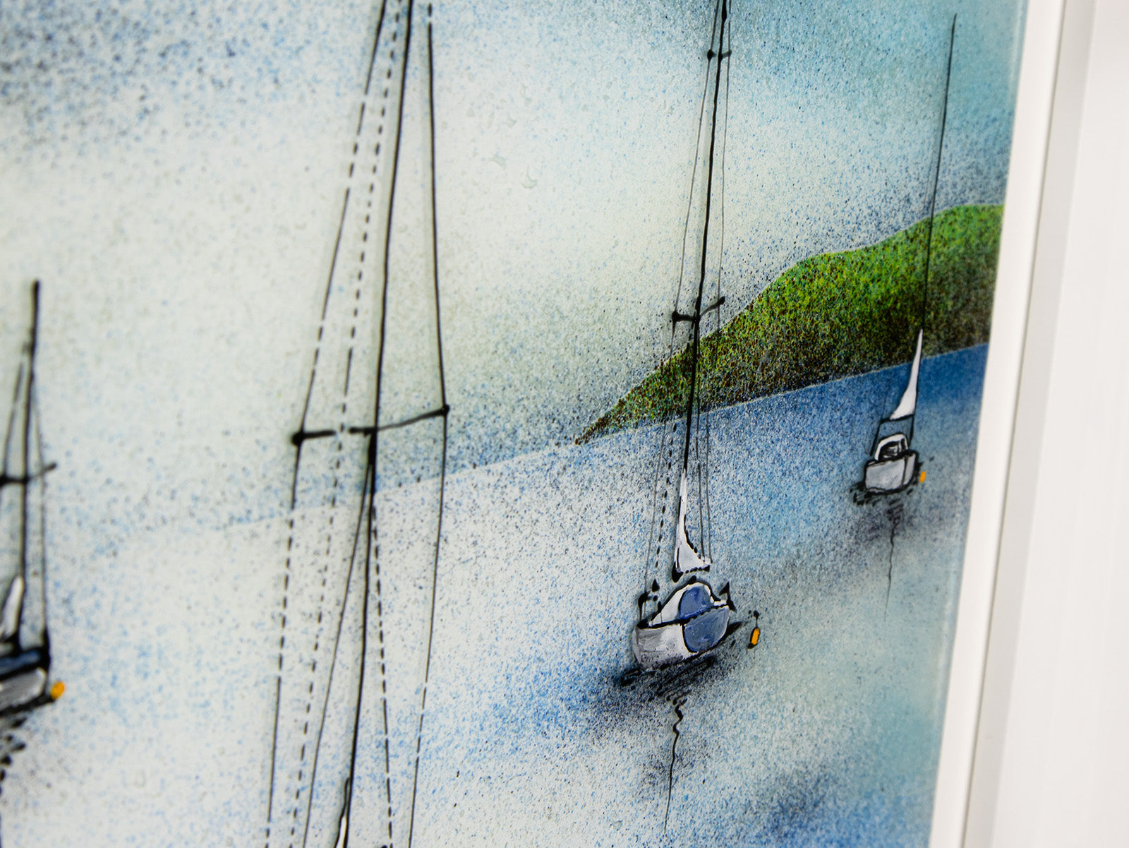 Details of a hand-painted fused glass design of several sailboats anchored, designed in soft coastal colours and presented in a white frame.
