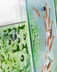 A detailed shot of a fused glass quintych featuring a soft coastal colour-way with darting copper fish and bubbled detailing. An ocean inspired piece of wall art. 