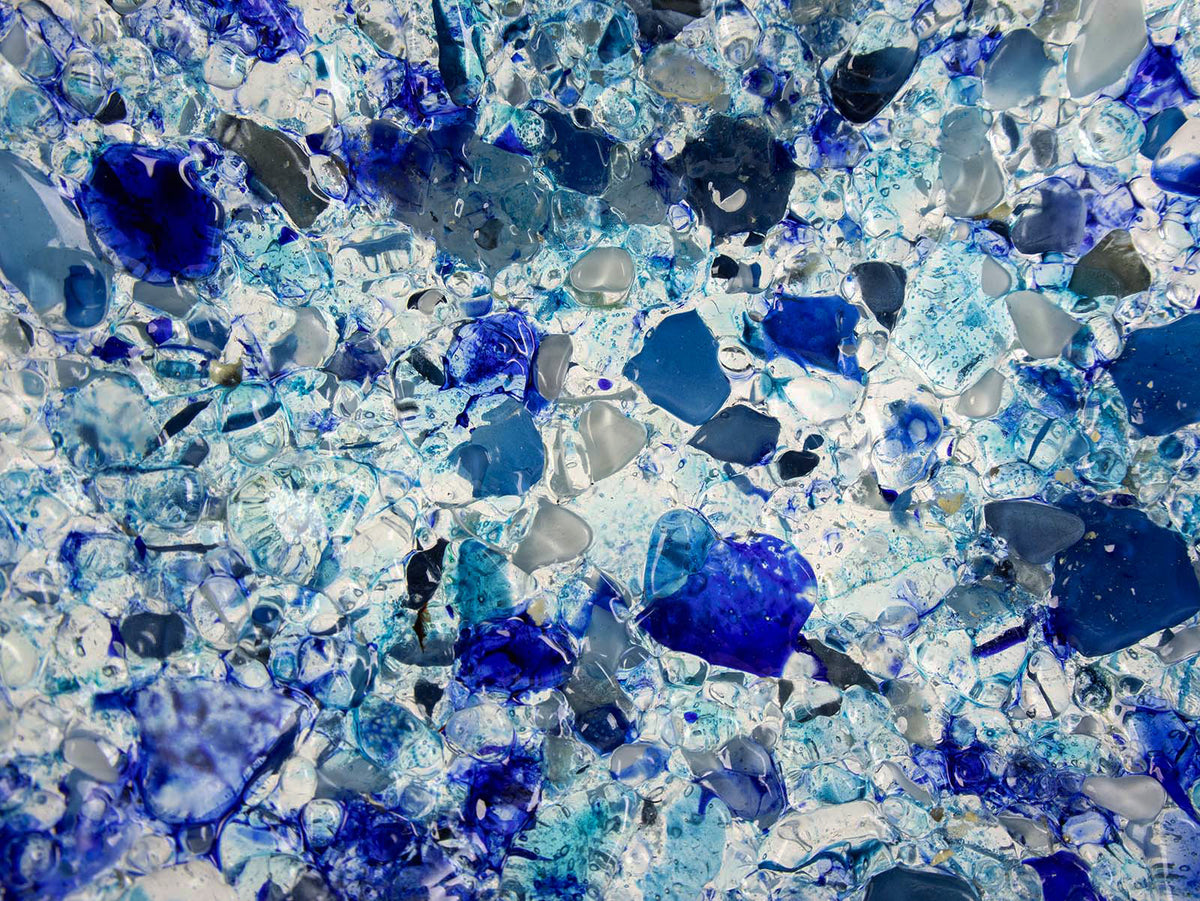 A close up of a fused glass round dish, handmade using recycled marine blue hues, designed to create a striking, ocean inspired piece of decor. 