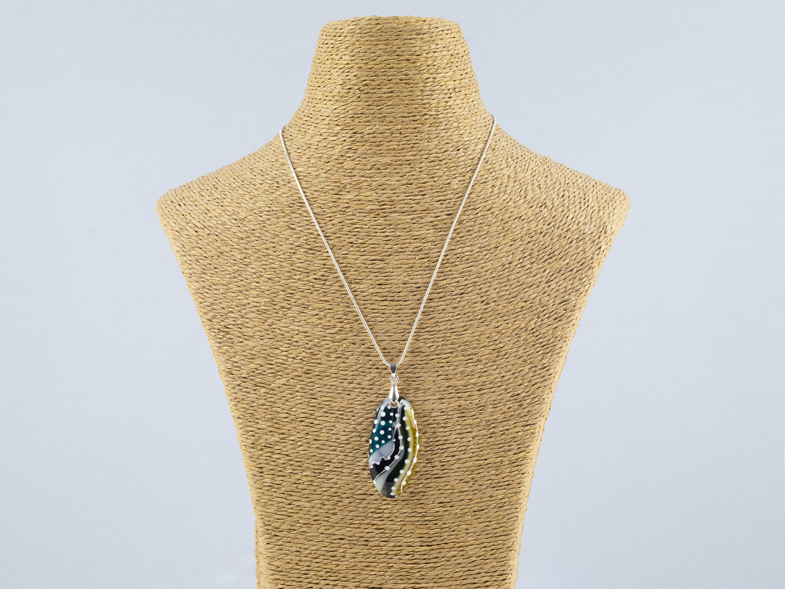 A fused glass pendant necklace on a sterling silver chain, handmade with soft coastal colours, with hand-painted dots and swirls. 
