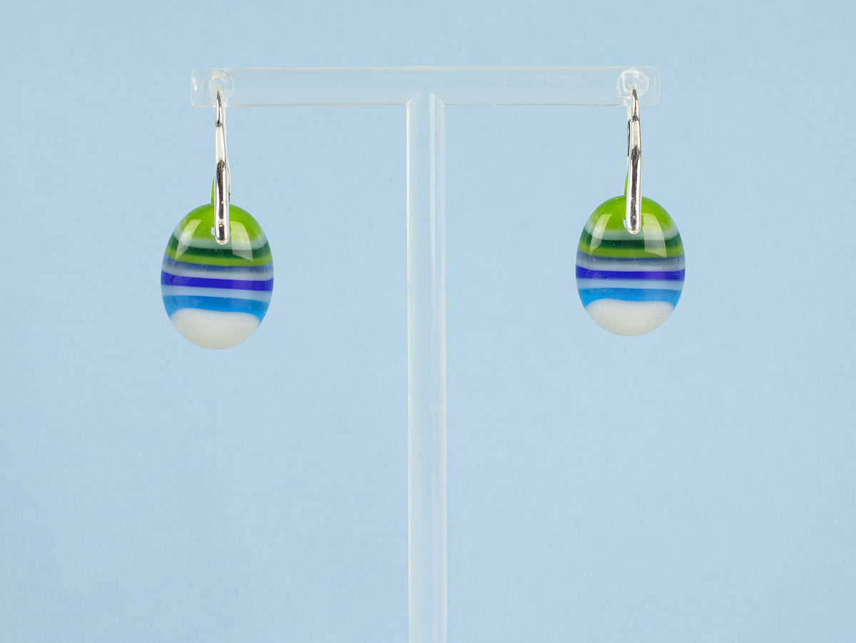 A pair of handmade glass drop earrings with green, blue, and white striped patterns, hanging from sterling silver fittings.