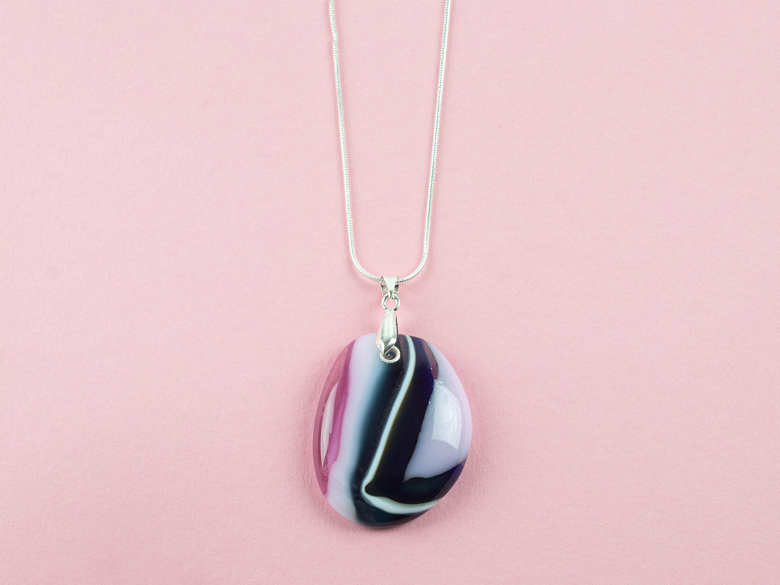 A fused glass pendant necklace hung on a sterling silver chain, handmade in heather pinks and organic deep hues. 