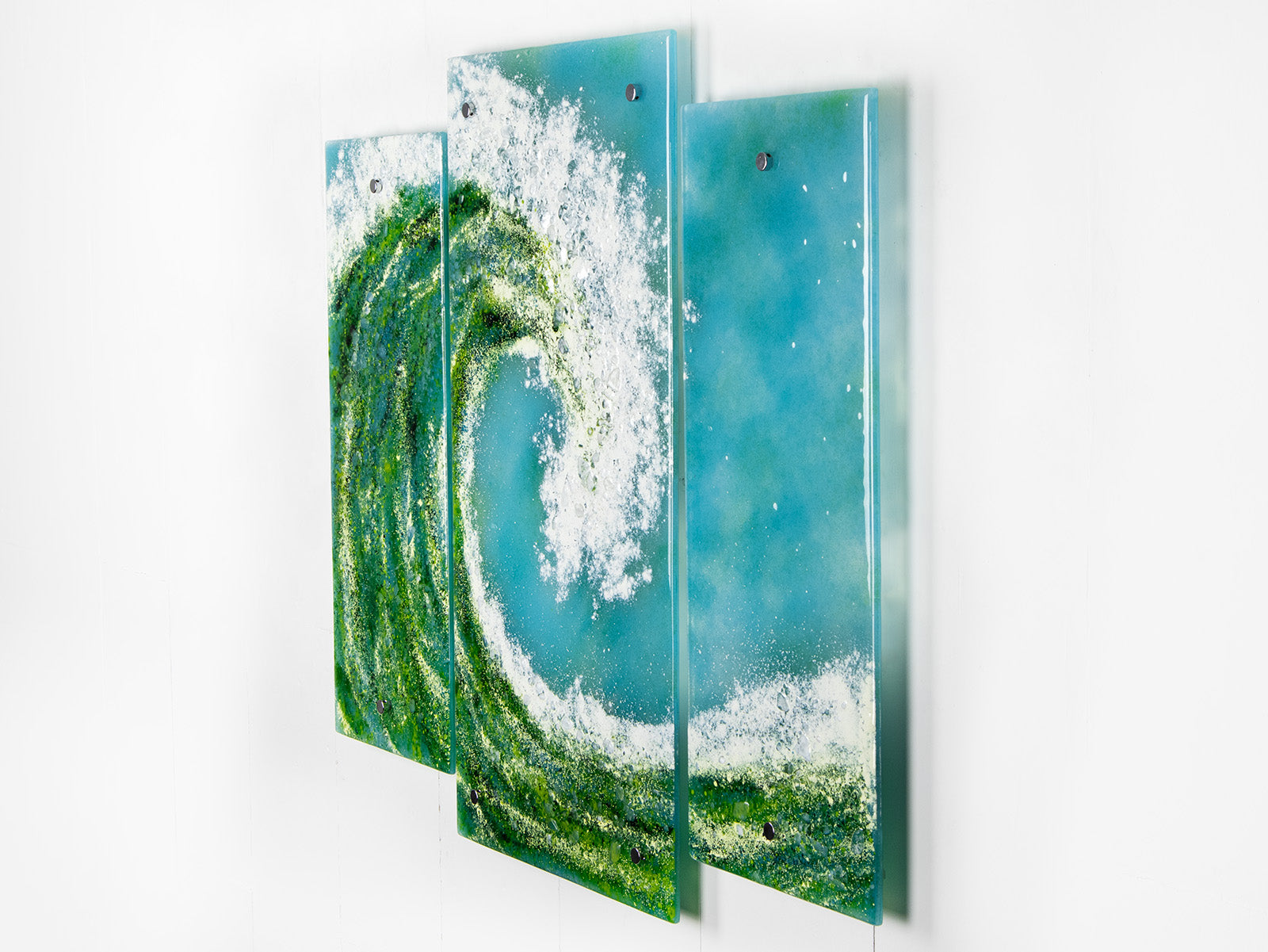 A fused glass triptych featuring a giant ocean wave, with aqua and sea green colours and white texture. 